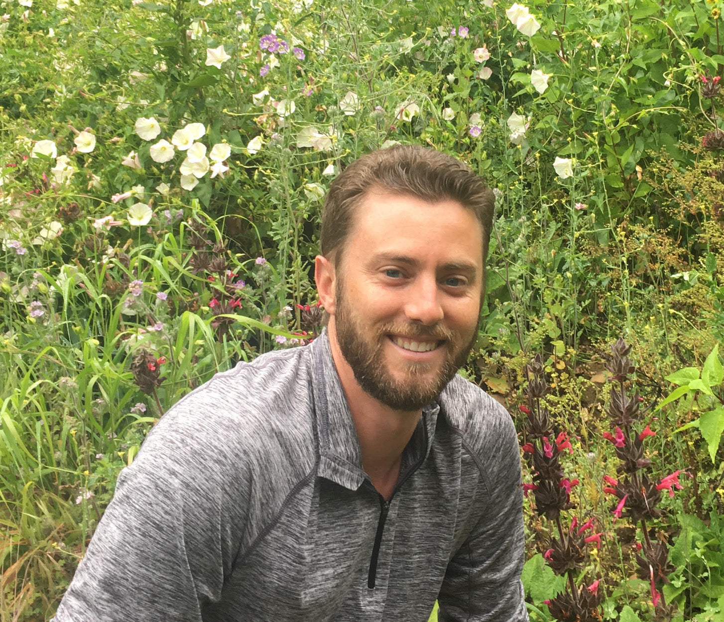 Man with a beard sitting in a garden with flowers and plants